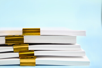 Many sheets of paper with golden clips on light blue background, closeup