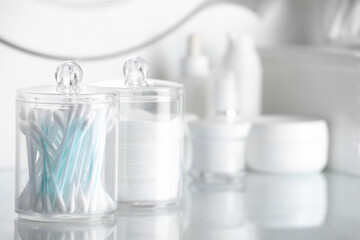 Containers with cotton swabs and pads near cosmetic products on dressing table. Space for text