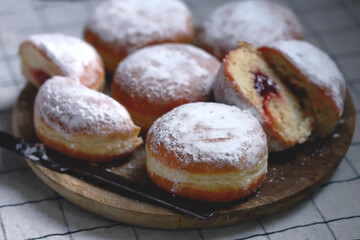 Berliner donuts in powdered sugar on a wooden tray.