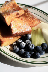 French toast with blueberries, kiwi and cream on white plate under sunlight. Morning coffee breakfast. French breakfast.