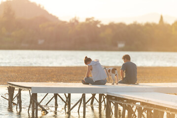 Fototapeta premium Romantic couple sitting at the beach with a dog. Happy romantic couple enjoying beautiful sunset at the beach