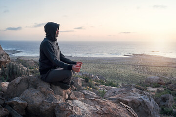 person meditating on a rock on the hill at sunset with the ocean in the background on the horizon