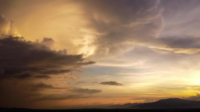 Aerial view of beautiful sky with clouds and sunlight during sunset. Time lapse of the clouds above the sky with the golden rays of the sun against the background of the silhouette of the mountain lan