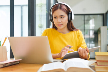 Woman learning online using laptop and writing notes.