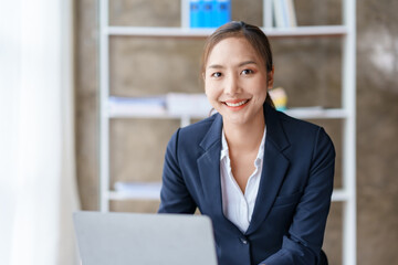 Fototapeta na wymiar Happy young asian businesswoman sitting on her workplace in the office. Young asian woman working at laptop in the office.