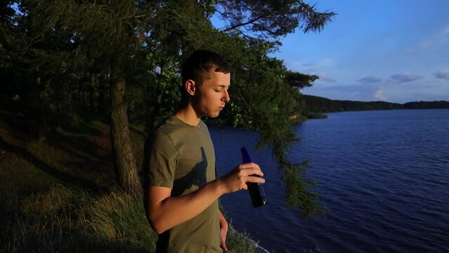 Young man having a beer and enjoying the sunset in the forest