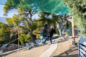 A man is resting in a rope amusement park. Front view.
