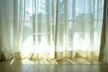 The curtain is attached behind the glass door with Two chairs, pine trees, sky and sunlight in the background. The curtains are thin and light cream colored fabrics. Use as sunscreen or for beauty.

