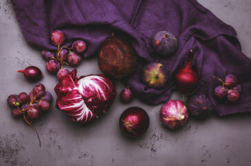 Autumn food background with purple vegetables, roots and fruits:: radicchio, beetroot, red onion, grapes, figs. Harvesting, local farm market shopping, healthy food concept. Top view