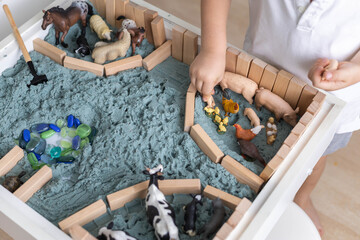 Cute baby boy playing sensory box kinetic sand table with farm animals