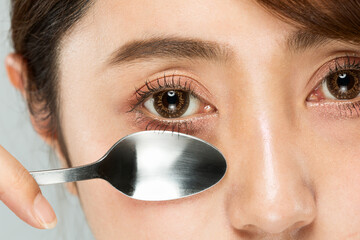 スプーンで目の下をマッサージする女性