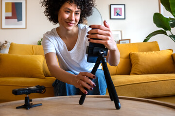 Smiling African American vlogger woman setting up mobile phone and voice recorder to film video for...