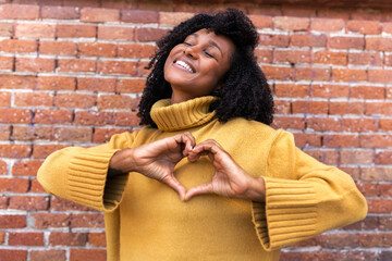 Happy, smiling young African American woman making heart shape with hands in front of chest.