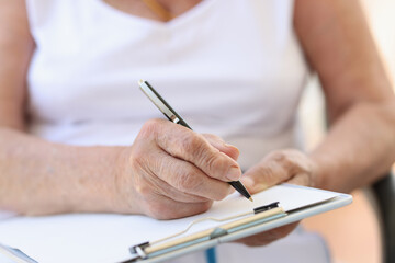 Old woman filling form with pen in clinic or in hospice