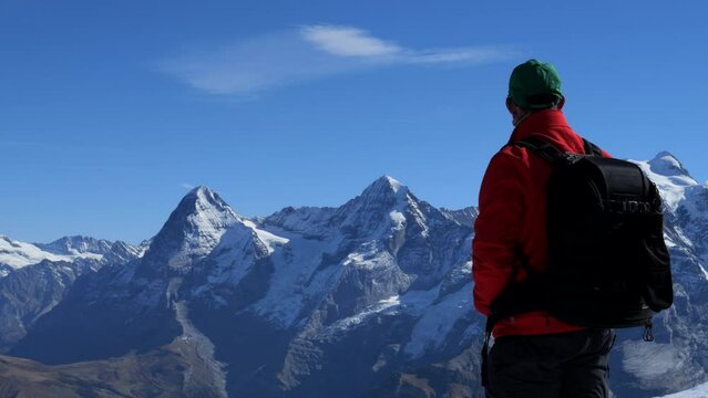 man in red coat enjoys the wonderful views and mountains of Jungfraujoch, known as top of Europe. A sunny day in the Swiss mountains.