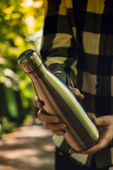Close-up of Unrecognizable female hand holding Water bottle. Reusable steel thermo water bottle in...