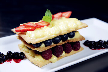Classic french dessert millefeuille with vanilla cream and fresh berries on a white plate. Millefeuille on isolated background. Side view