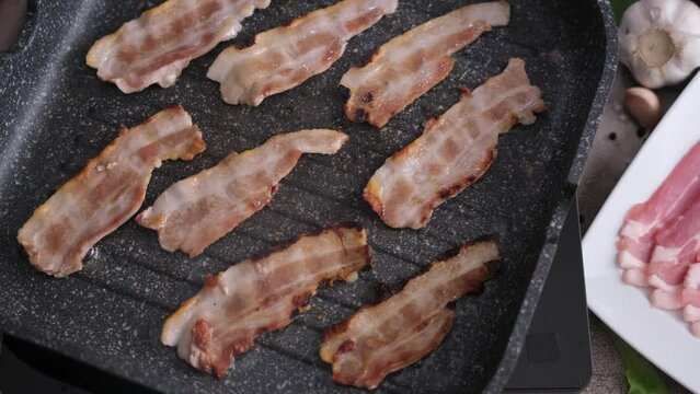 cooking Pieces of flavorful sliced organic bacon fried in a grill pan