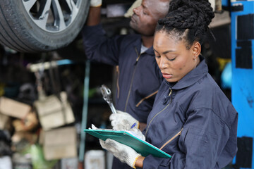 Group of car mechanic in uniform checking maintenance a lifted car service with clipboard at repair garage station. Worker holding wrench and fixing breakdown vehicle. Car repair service concept