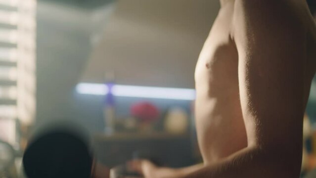 Muscular young boy do dumbbells curls in his room. Closeup of his biceps and muscular abs. Checks his muscles in the mirror. Weight training, fitness, physical activity. Healthy lifestyle concept.