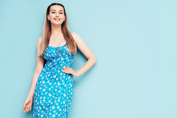 Portrait of young beautiful smiling female in trendy summer dress. Sexy carefree woman posing near blue wall in studio. Positive model having fun and going crazy. Cheerful and happy