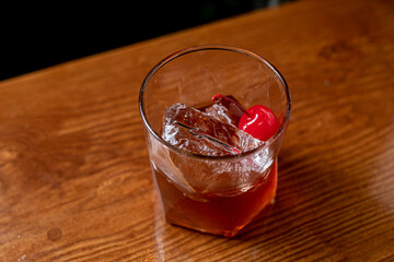 Old-fashioned drink at bar with a slice of orange, cherry and ice, a classic alcoholic drink