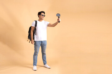 Young Asian tourist backpacker man smiling and taking a selfie and blog isolated on beige background - 537166394