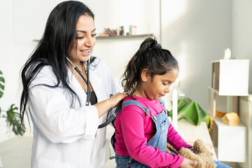 female doctor Hispanic pediatrician auscultating a small child - health concept -