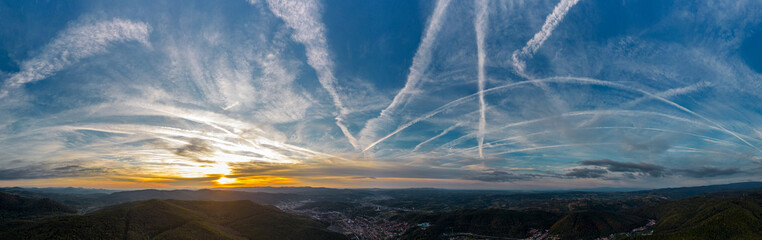Aerial panorama view of colorful autumn sunset with visible airplane contrails, over Resita city, Romania. Captured from a drone.