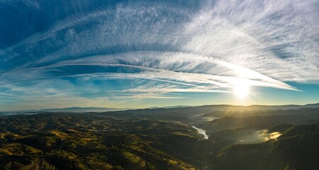 Aerial panorama view of a foggy sunrise with visible airplane contrails in a hilly area near Resita city, Romania. Captured with a drone - obrazy, fototapety, plakaty