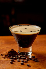 
delicioso martini espresso en un vaso junto a granos de café sobre una mesa de madera