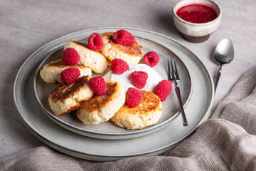 Cheesecakes or syrniki on a round plate with raspberry, sour cream and raspberry syrup.Healthy...