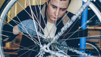 Concentrated handsome guy skilled mechanic is repairing bicycle wheel with wrenchwhile working in his workplace. Bike maintenance, people and profession concept.