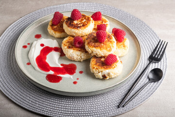 Cheesecakes or syrniki on a round plate with raspberry, sour cream and raspberry syrup.Healthy breakfast. Delicious dessert.