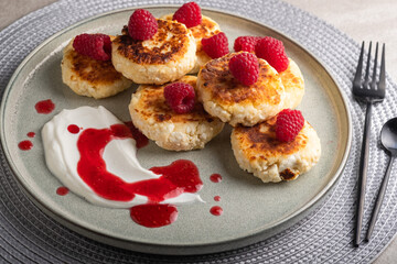 Cheesecakes or syrniki on a round plate with raspberry, sour cream and raspberry syrup.Healthy breakfast. Delicious dessert.