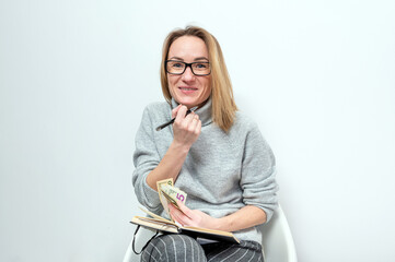 blond woman with glasses counting money and writing in a notebook, isolated on a gray