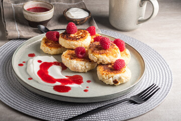 Cheesecakes or syrniki on a round plate with raspberry, sour cream and raspberry syrup.Healthy breakfast. Delicious dessert.
