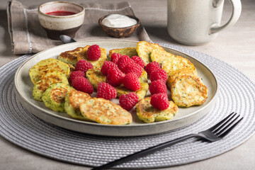 Gluten-free zucchini pancakes with fresh raspberries, raspberry jam, sour cream on a round grey plate.  Healthy food concept, summer food.