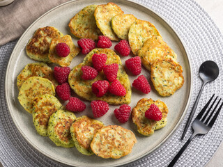 Gluten-free zucchini pancakes with fresh raspberries, raspberry jam, sour cream on a round grey plate.  Healthy food concept, summer food.