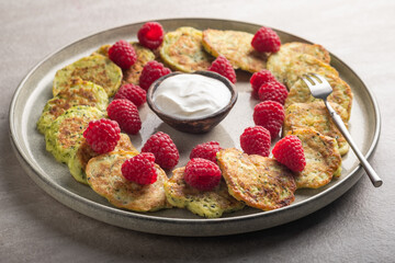 Gluten-free zucchini pancakes with fresh raspberries, raspberry jam, sour cream on a round grey plate.  Healthy food concept, summer food.