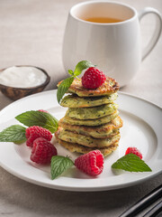 Stack of fresh homemade zucchini pancakes topped with raspberries and sour cream. Green tea in a white cup.