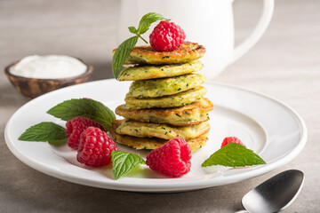 Stack of fresh homemade zucchini pancakes topped with raspberries and sour cream. Green tea in a white cup.