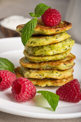 Stack of fresh homemade zucchini pancakes topped with raspberries and sour cream. Green tea in a white cup.