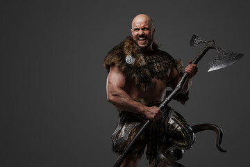 Portrait of furious nordic warrior with muscular build dressed in armor holding axe.
