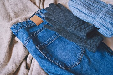 Winter clothes outfit. Comfy women's clothing. Beige sweater, blue jeans, knitted hat and gray gloves 