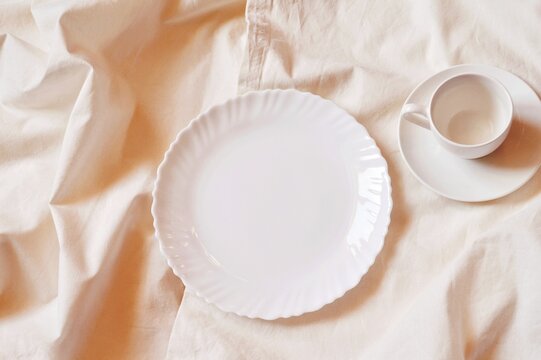 White new dishes on the table. Empty porcelain plate and small coffee cup and saucer. Flat lay photography, top view image, mockup