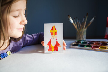 girl shows children's drawing - card for day of saint nicholas on table background for traditional Dutch holiday sinterklaas. craft for kids