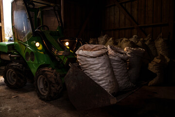 Fototapeta na wymiar Shot of green tractor transporting bags of potatoes in hangar of farm.