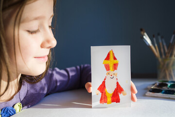 girl shows children's drawing - card for day of saint nicholas on table background for traditional Dutch holiday sinterklaas. craft for kids
