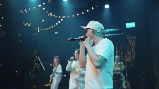 cool rapper is rapping on stage, concert of popular hip-hop band, musicians playing live music
